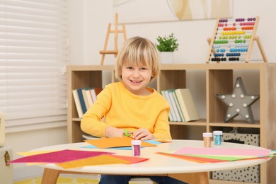 Photo of Cute little boy cutting orange paper at desk in room. Home workplace
