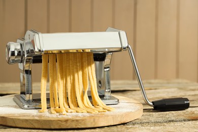 Pasta maker with raw dough on wooden table