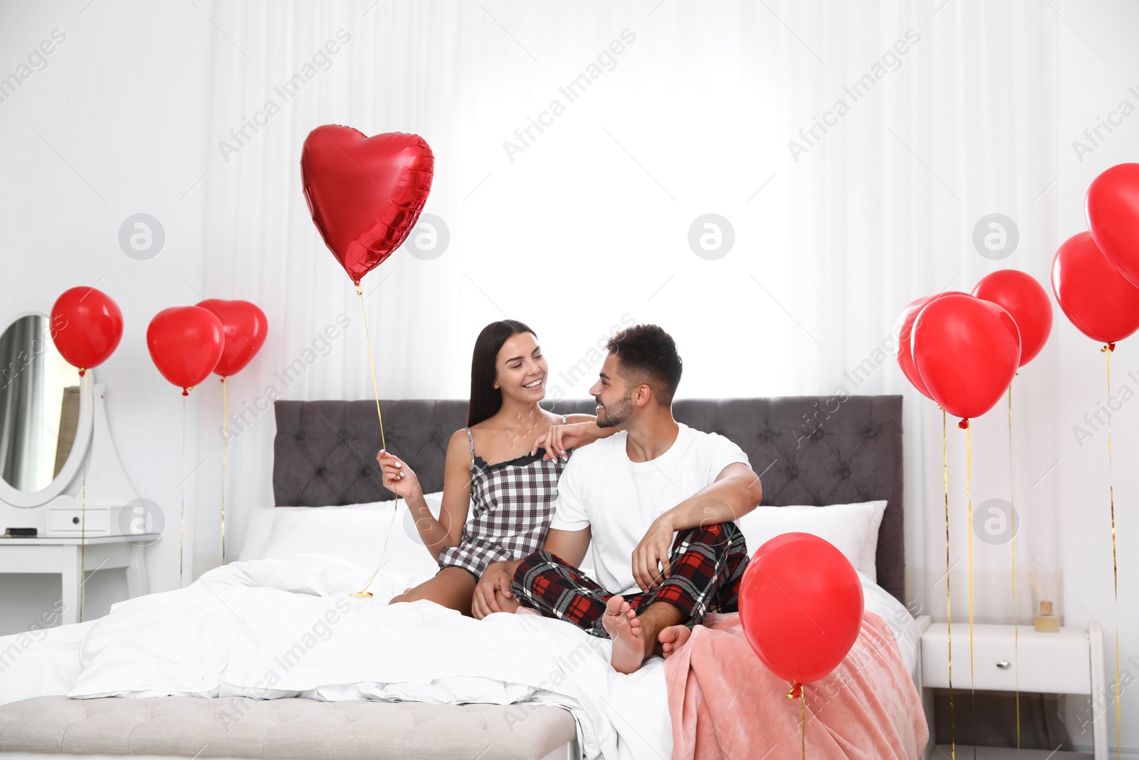 Photo of Young couple in bedroom decorated with air balloons. Celebration of Saint Valentine's Day