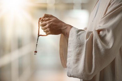 Image of Muslim man with misbaha praying on blurred background, closeup