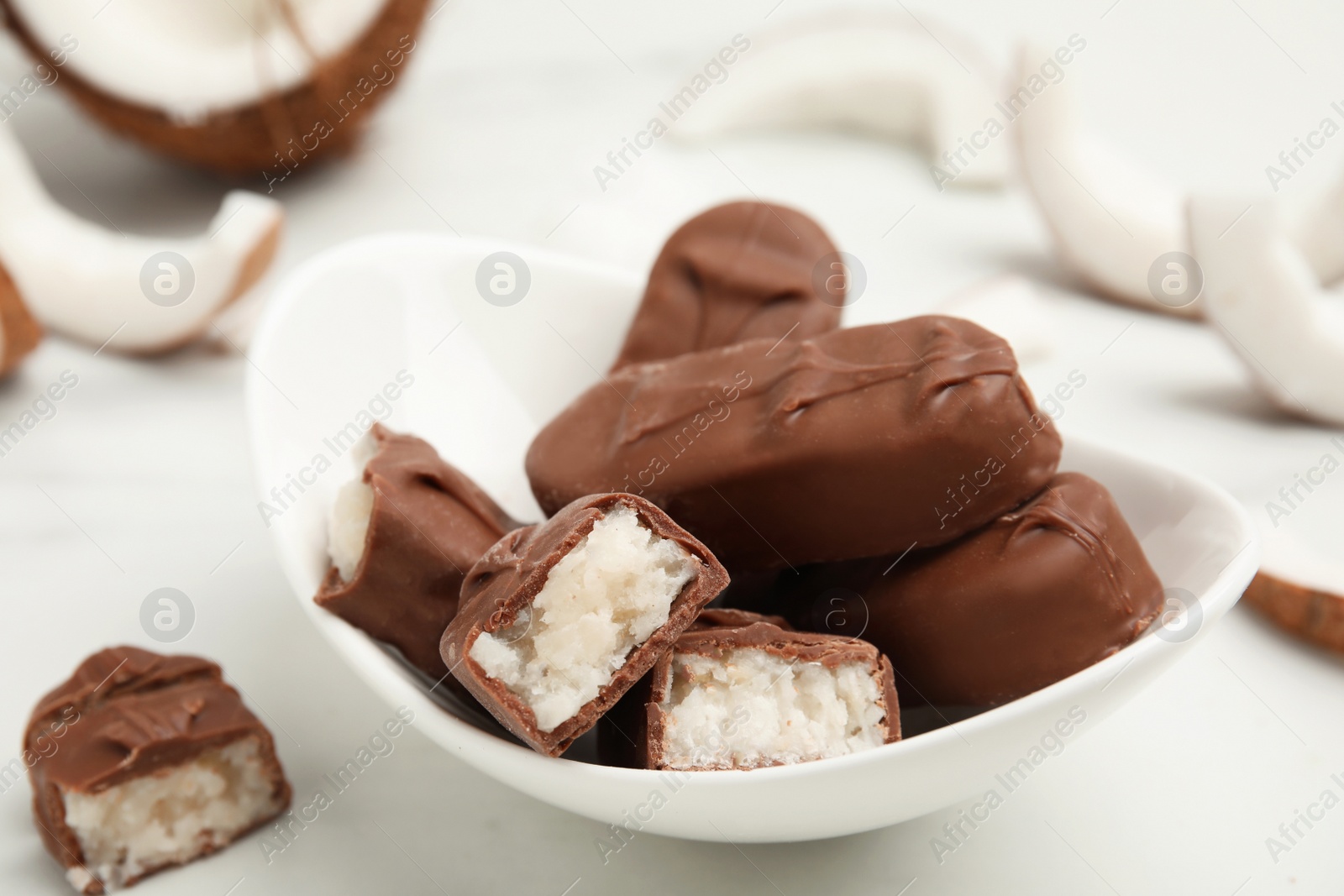 Photo of Delicious milk chocolate candy bars with coconut filling on white table, closeup