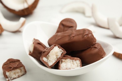 Delicious milk chocolate candy bars with coconut filling on white table, closeup