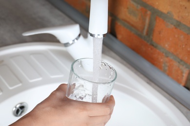 Woman filling glass with water from faucet in kitchen, closeup