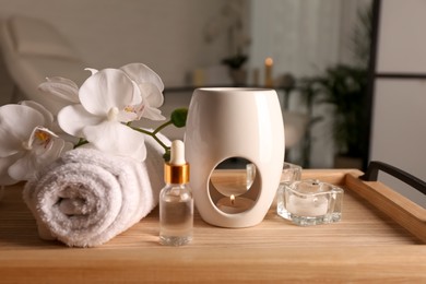 Photo of Aroma lamp, bottleoil, rolled towel and candles on wooden tray indoors