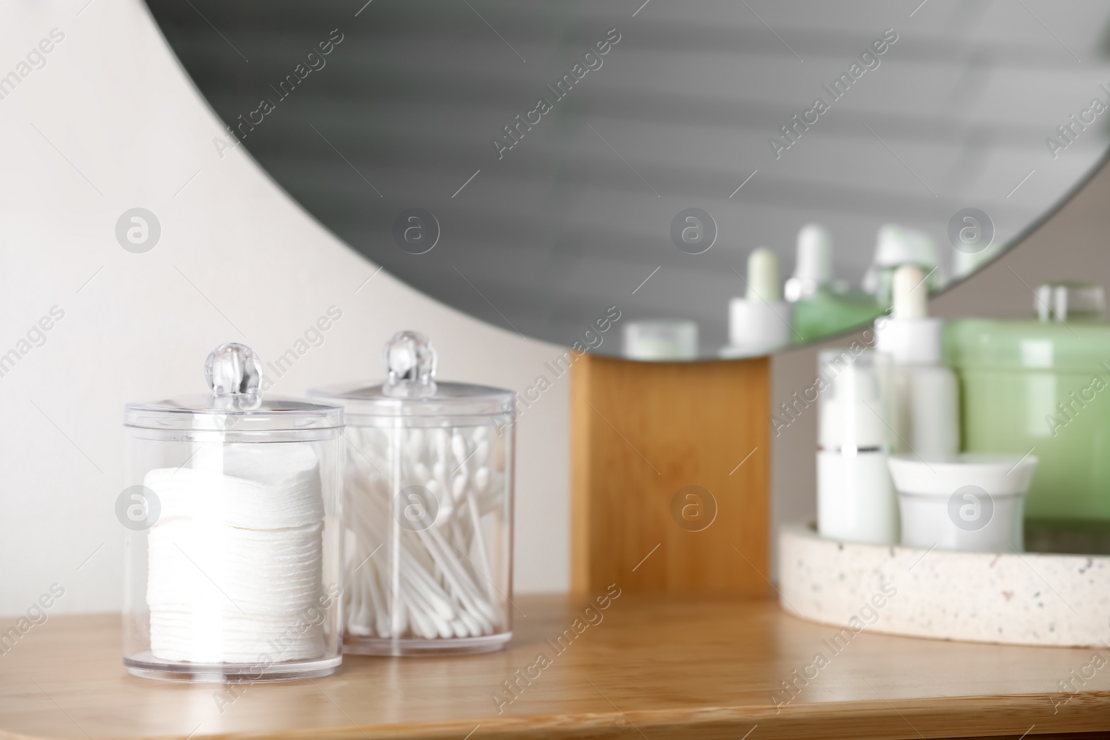 Photo of Containers with cotton swabs and pads near cosmetic products on dressing table