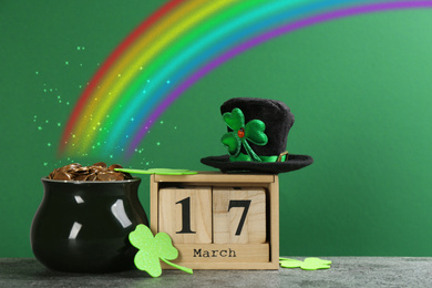 Pot with gold coins, wooden block calendar, hat and cloverleaves on table against green background. St. Patrick's Day celebration