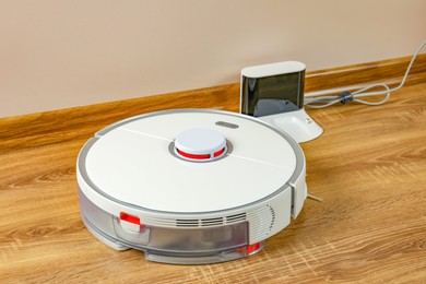 Photo of Robotic vacuum cleaner and charger on wooden floor indoors