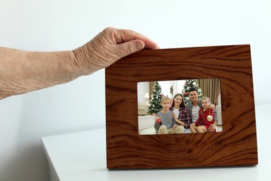 Elderly woman with framed photo portrait of her family indoors, closeup