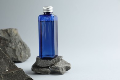 Photo of Bottle of cosmetic product on stones against light grey background, space for text