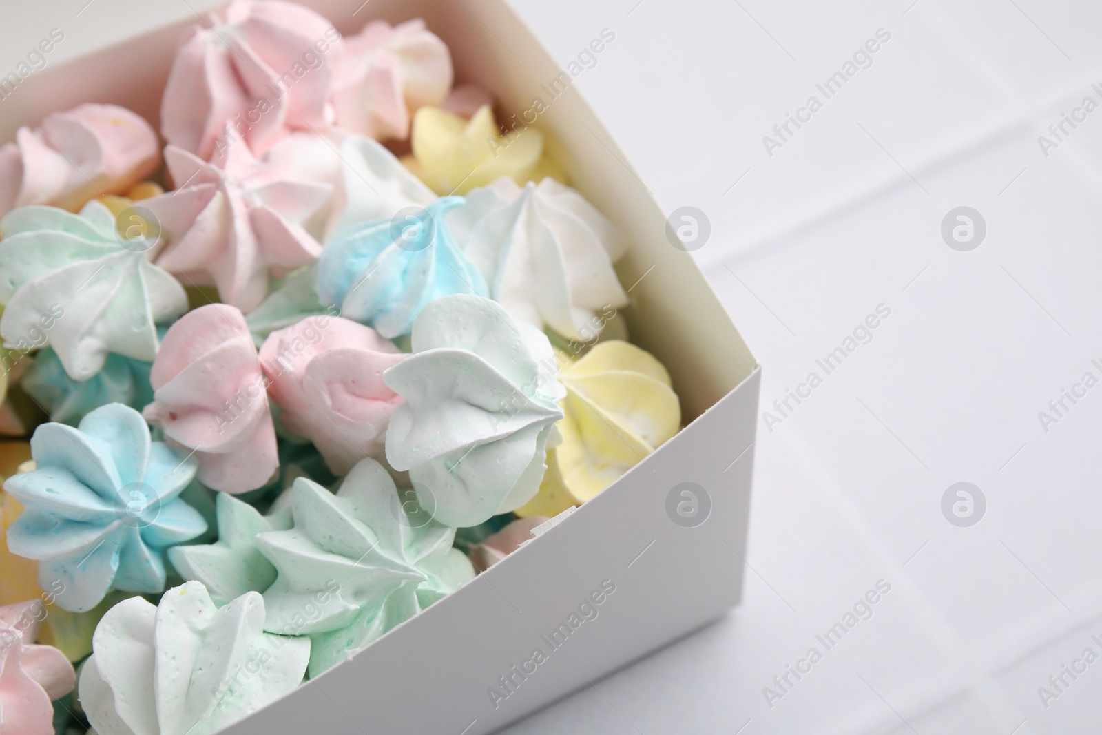 Photo of Tasty meringue cookies on white tiled table, closeup. Space for text