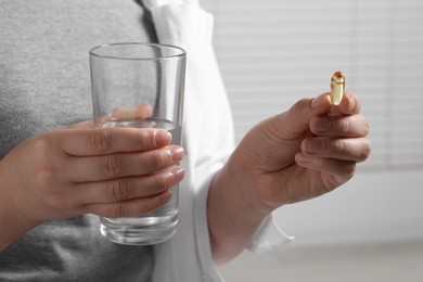 Woman with glass of water and pill on light background, closeup