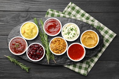 Photo of Different tasty sauces in bowls and rosemary on black wooden table, top view