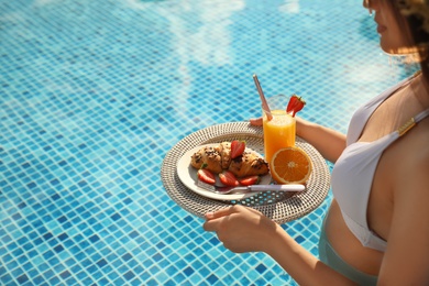 Photo of Young woman with delicious breakfast on tray in swimming pool, closeup. Space for text