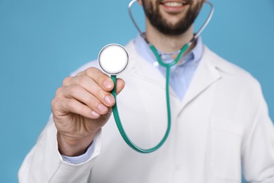 Photo of Doctor with stethoscope on light blue background, closeup. Cardiology concept