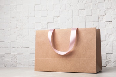 Photo of Paper shopping bag with ribbon handles on table near white wall. Mockup for design