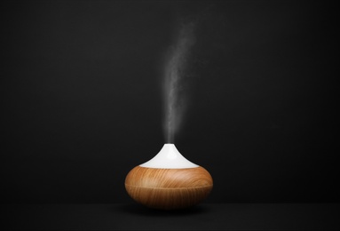 Modern essential oil diffuser on black background. Space for text