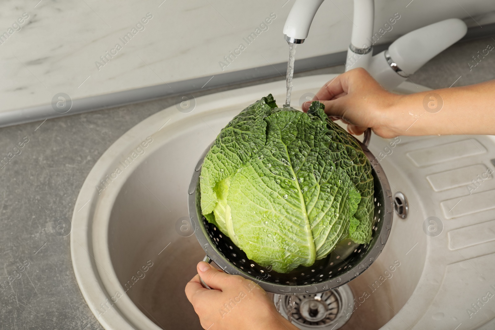 Photo of Woman washing savoy cabbage in colander under tap water, closeup