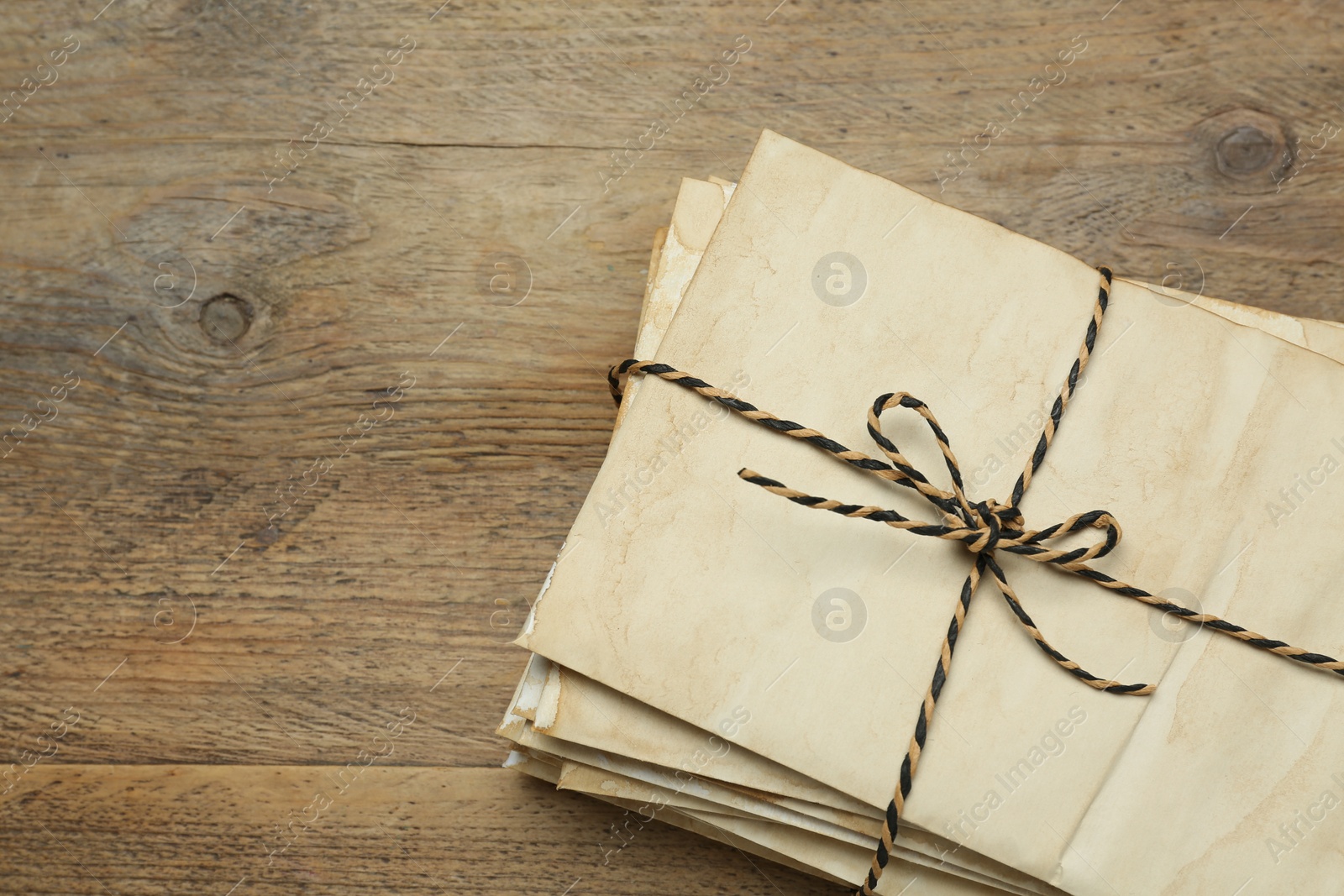 Photo of Stack of old letters tied with string on wooden table, top view. Space for text