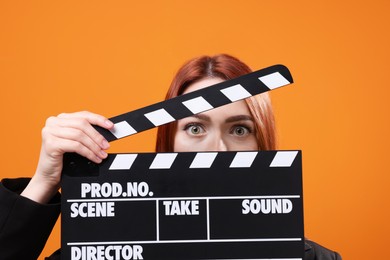 Photo of Emotional actress with clapperboard on orange background. Film industry
