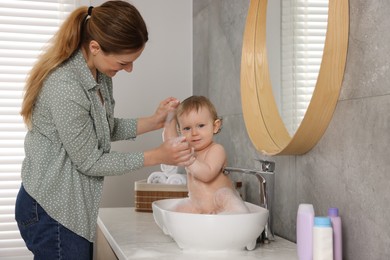 Photo of Mother washing her little baby in sink at home