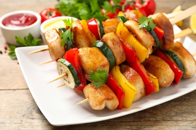 Photo of Delicious chicken shish kebabs with vegetables on wooden table, closeup