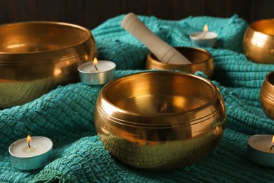 Photo of Tibetan singing bowls with mallet and burning candles on turquoise fabric