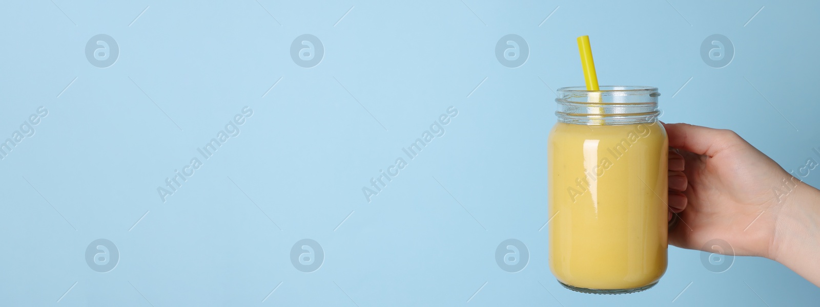 Image of Woman holding mason jar with tasty smoothie and straw on light blue background, closeup view ,with space for text. Banner design