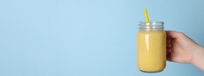 Woman holding mason jar with tasty smoothie and straw on light blue background, closeup view ,with space for text. Banner design