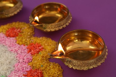 Photo of Diwali celebration. Diya lamps and colorful rangoli on purple background, closeup