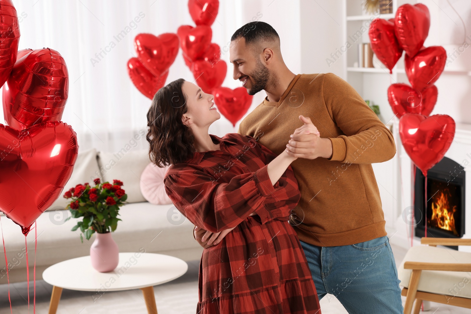 Photo of Lovely couple dancing in room decorated with heart shaped air balloons. Valentine's day celebration