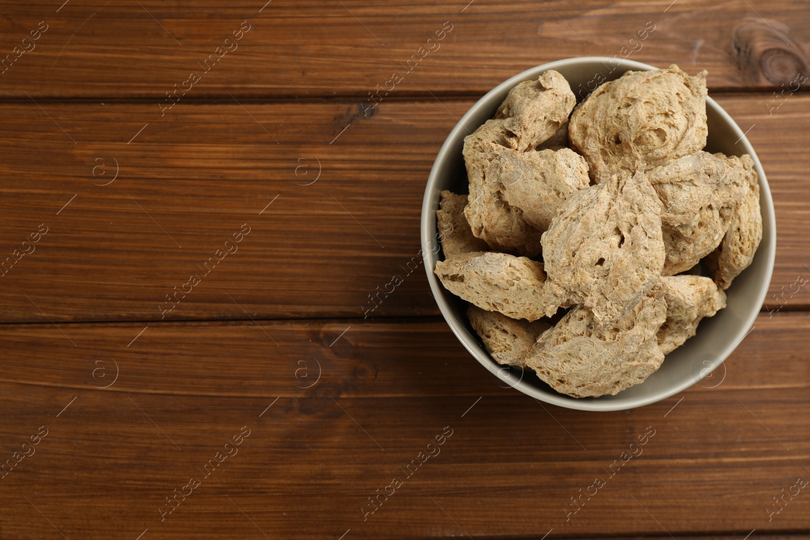 Photo of Dehydrated soy meat chunks in bowl on wooden table, top view. Space for text