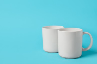 Two white ceramic mugs on light blue background, space for text