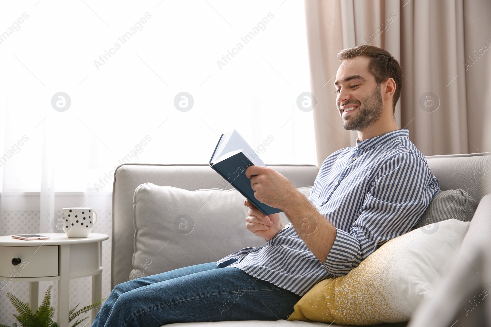 Photo of Handsome young man reading book on sofa at home