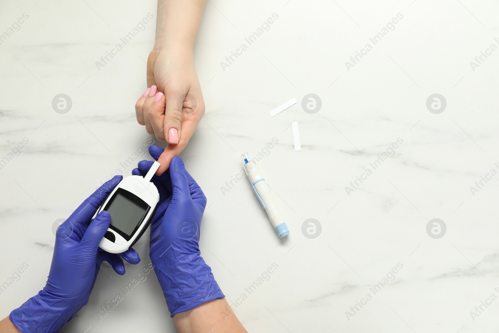 Photo of Diabetes. Doctor checking patient's blood sugar level with glucometer at white marble table, top view. Space for text