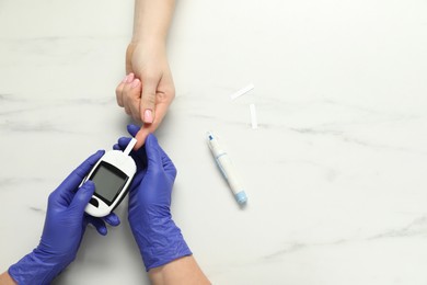 Photo of Diabetes. Doctor checking patient's blood sugar level with glucometer at white marble table, top view. Space for text