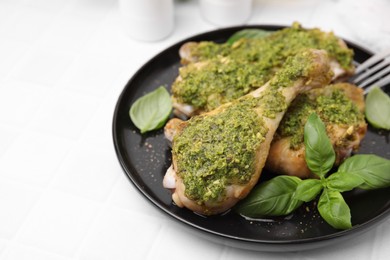 Photo of Delicious fried chicken drumsticks with pesto sauce and basil on white table, closeup. Space for text