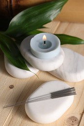 Photo of Stones with acupuncture needles and burning candle on wooden table