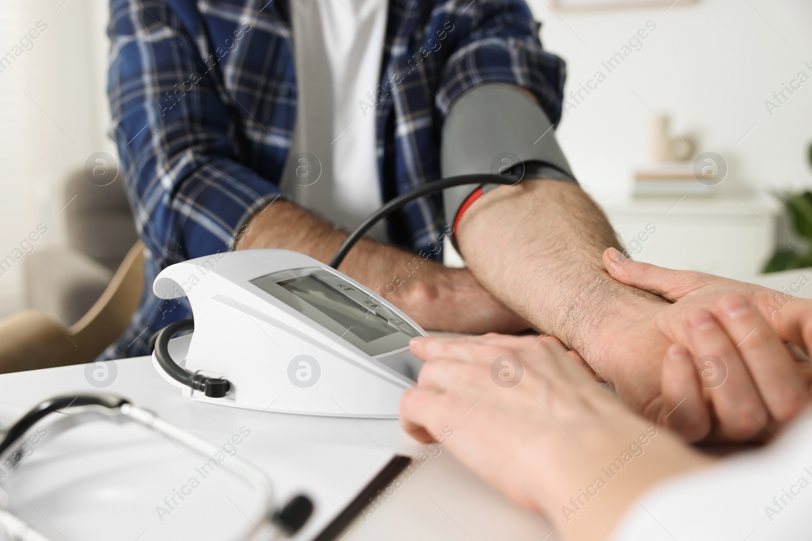 Photo of Doctor measuring blood pressure of man at table indoors, closeup