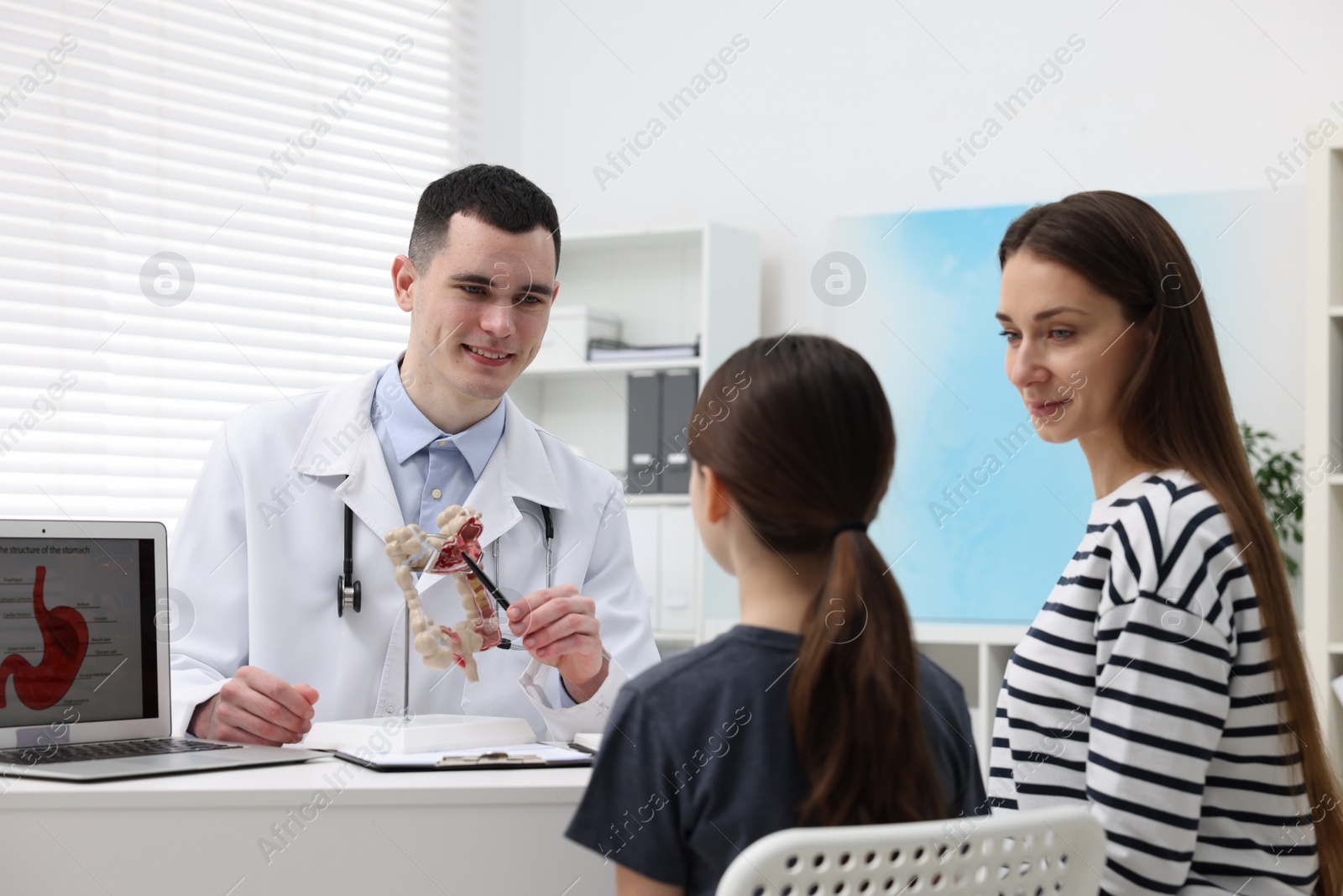 Photo of Gastroenterologist with model of intestine consulting woman and her daughter in clinic