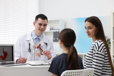 Gastroenterologist with model of intestine consulting woman and her daughter in clinic