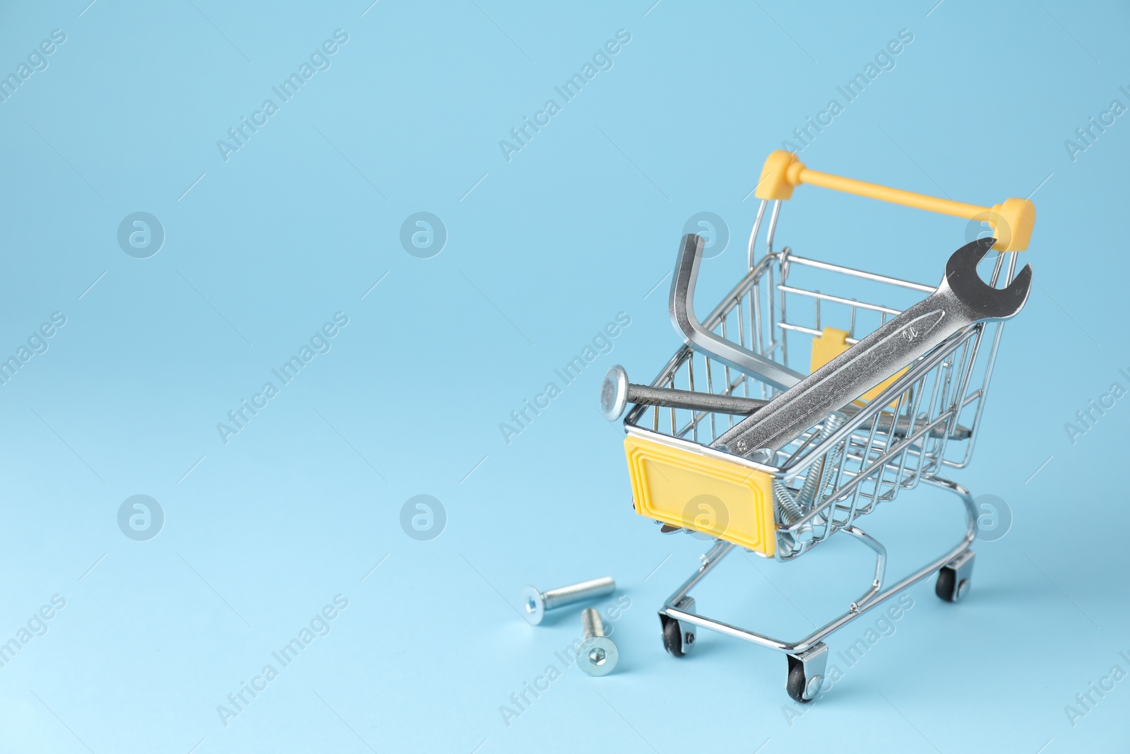 Photo of Different construction tools in shopping cart on light blue background, space for text