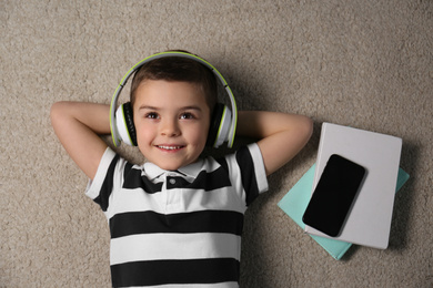 Photo of Cute little boy listening to audiobook on floor, top view