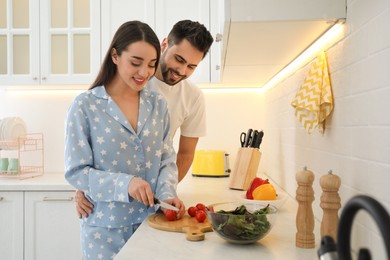 Photo of Happy couple in pajamas cooking at kitchen counter