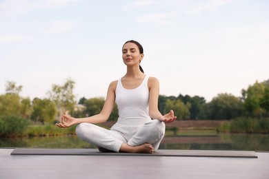 Photo of Beautiful young woman practicing Padmasana on yoga mat outdoors, low angle view. Lotus pose