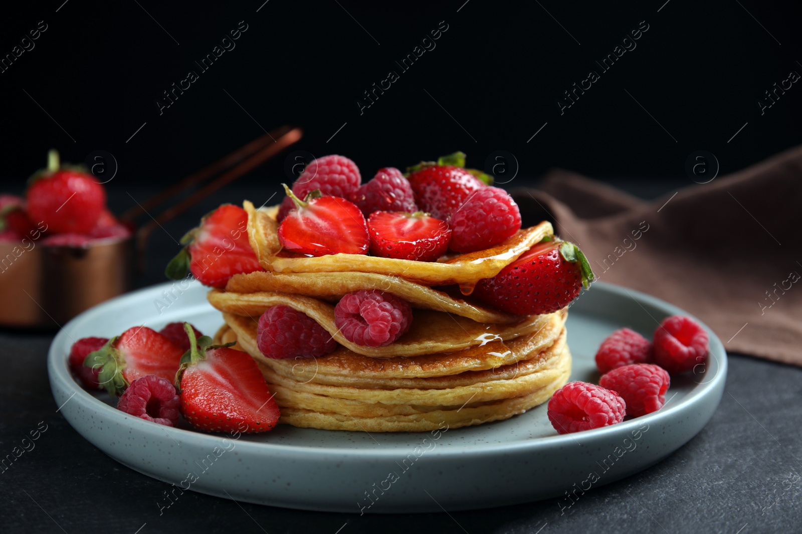 Photo of Tasty pancakes with fresh berries and honey on black table, closeup