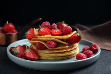 Tasty pancakes with fresh berries and honey on black table, closeup