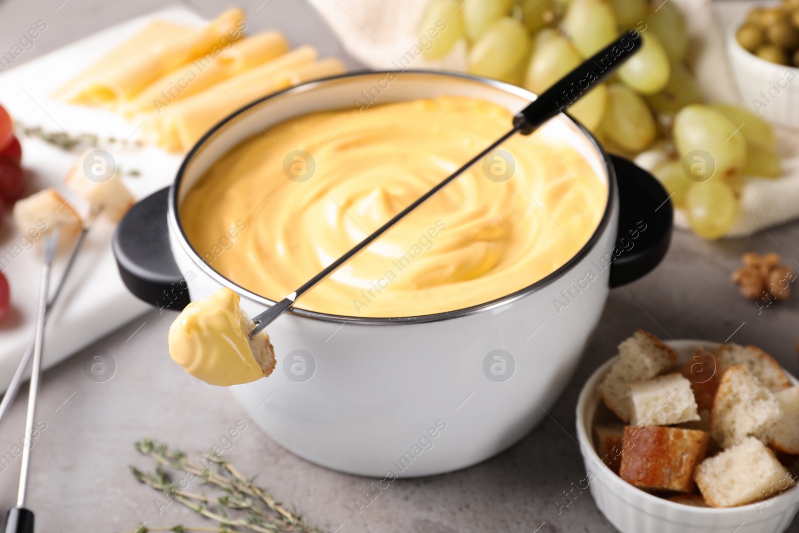 Photo of Pot of delicious cheese fondue and fork with bread on gray table