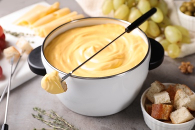 Photo of Pot of delicious cheese fondue and fork with bread on gray table