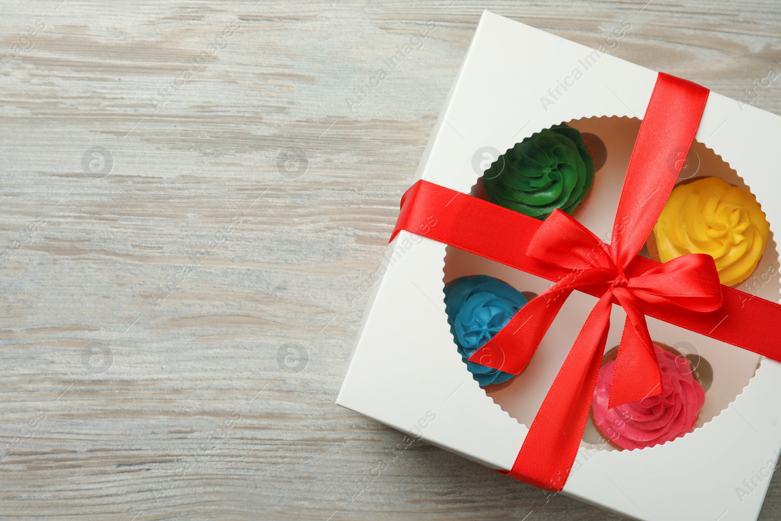 Photo of Box with delicious colorful cupcakes on white wooden table, top view. Space for text