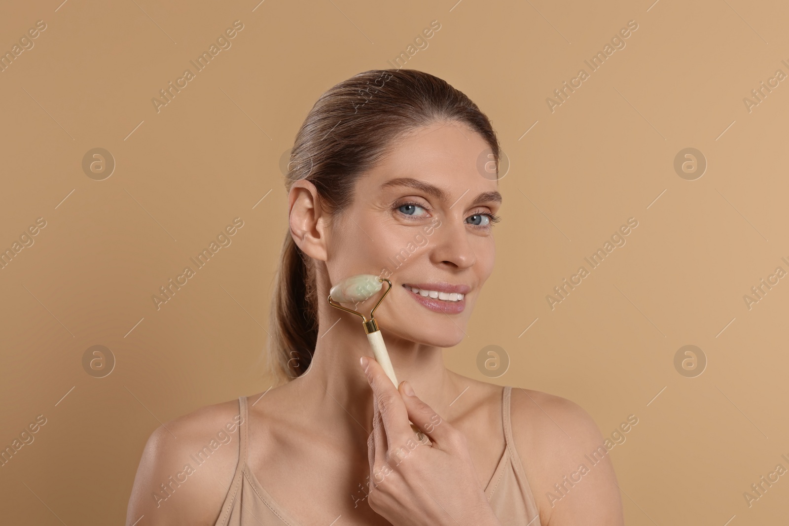 Photo of Woman massaging her face with jade roller on beige background